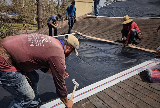 Men working on nailing a billboard tarp to the roof of a house