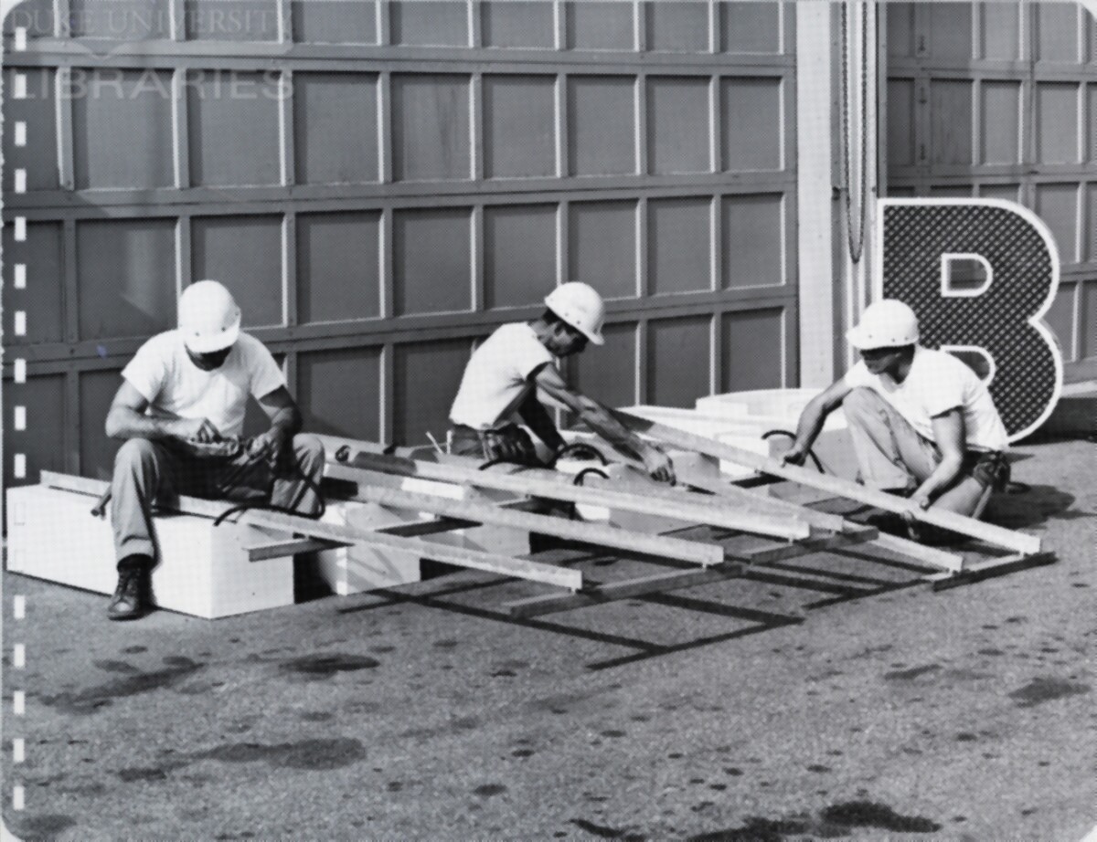 Three men position supports on lettering for a billboard.