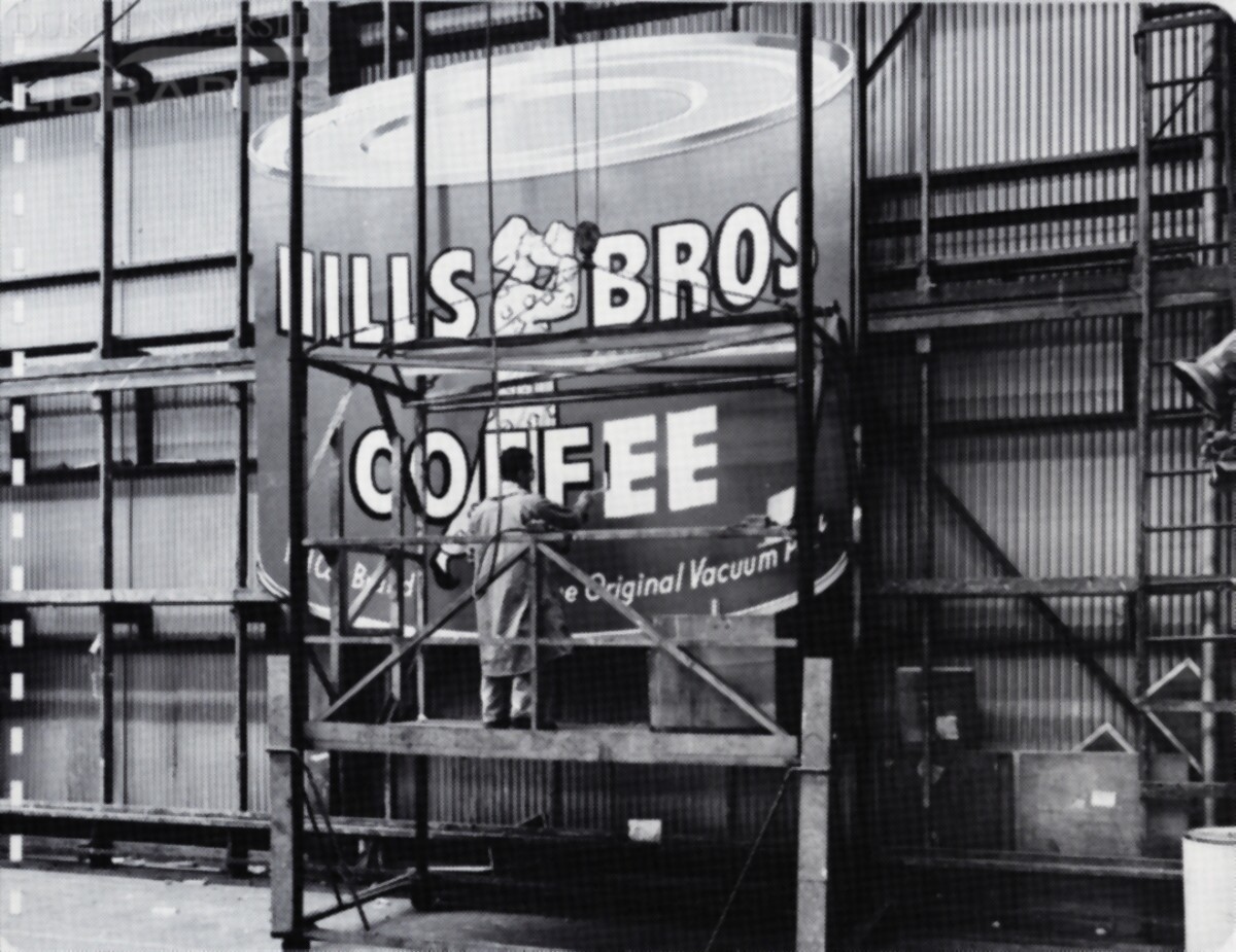 A painter details lettering on a huge replica of a coffee can.