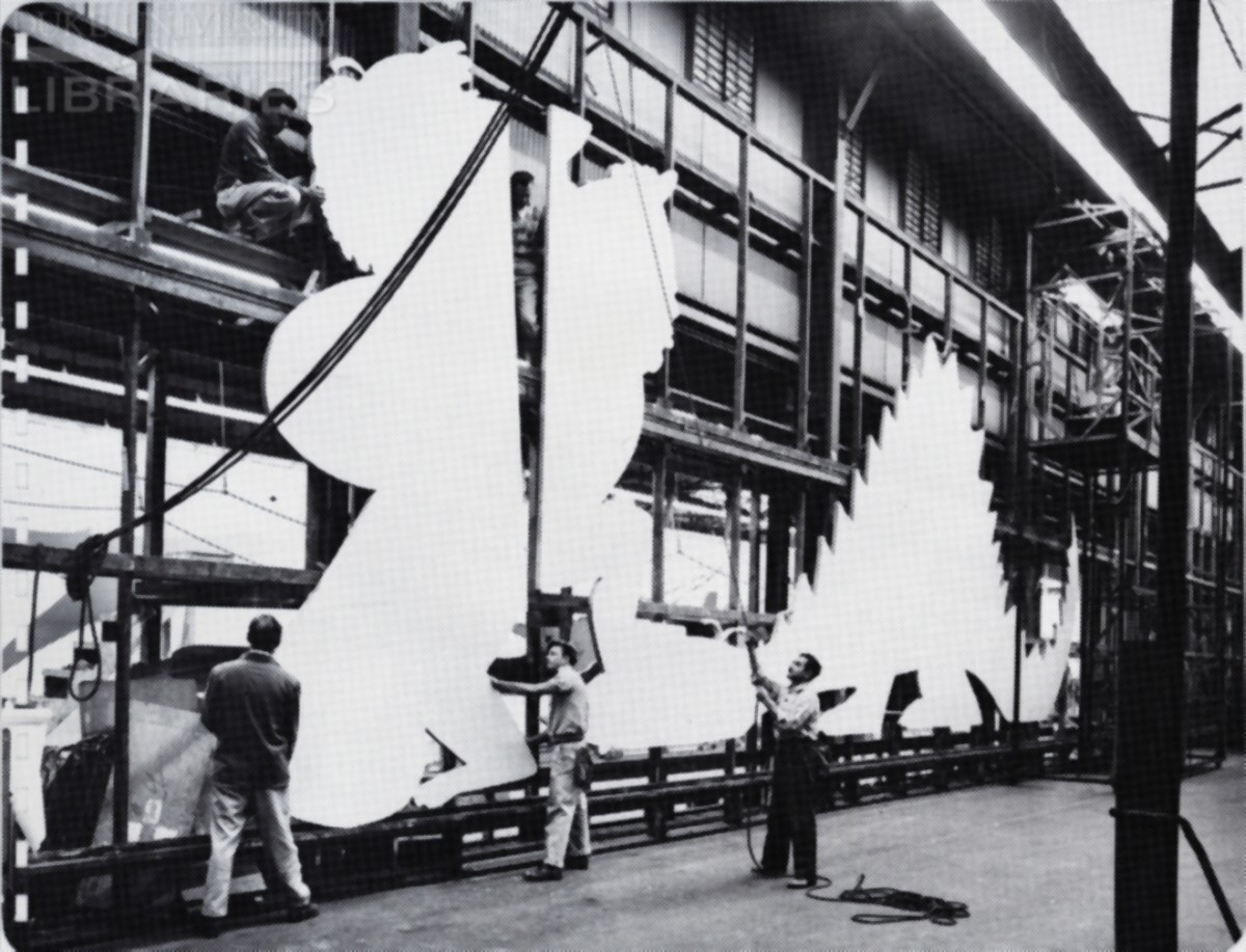 A crew of men is positioning large wooden billboard cutouts along a frame wall as part of the finishing process.