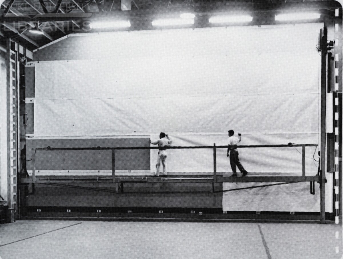 Two men laying out paper to make a full-size billboard design.