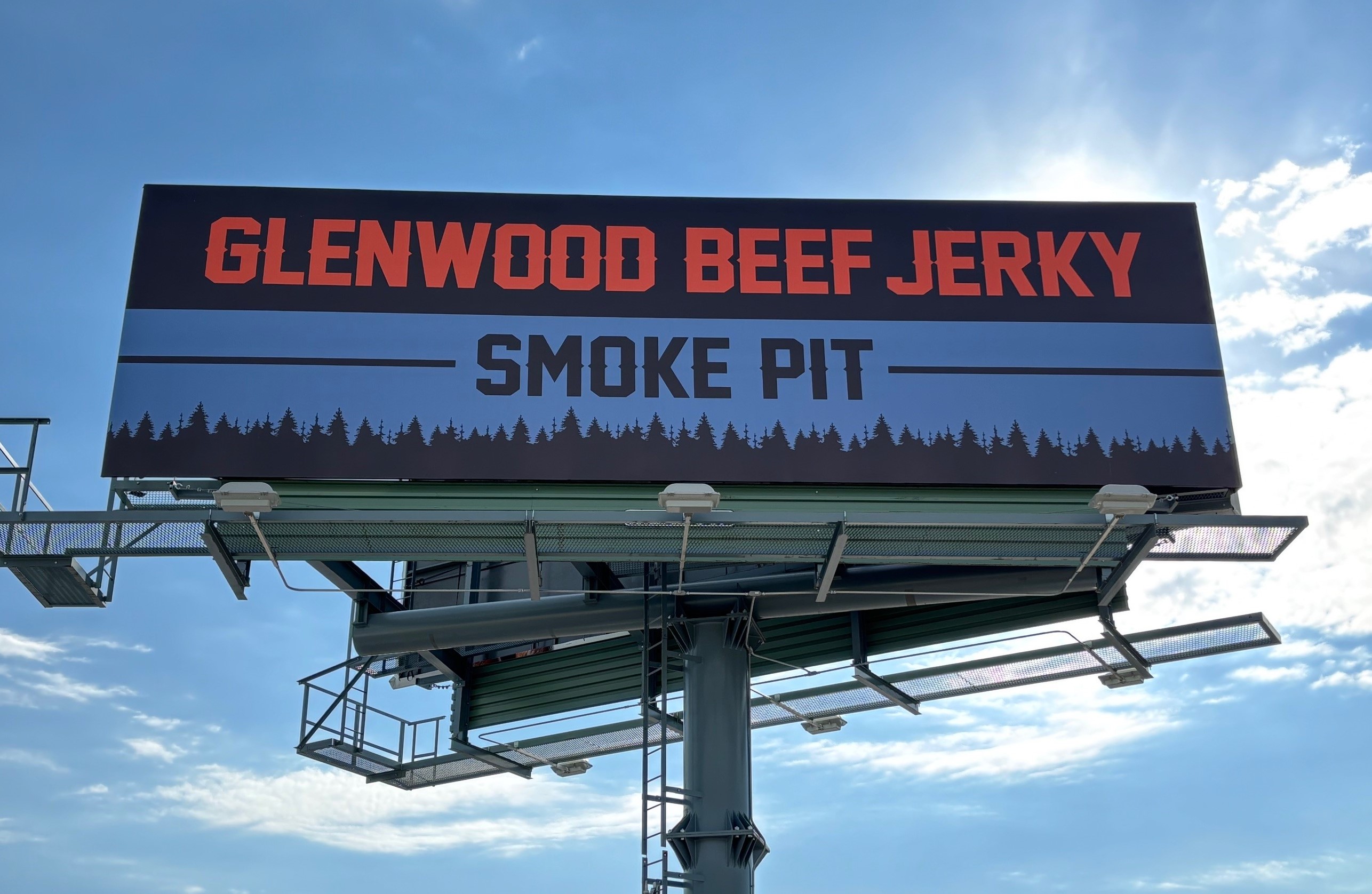 Glenwood Beef Jerky billboard that is blue, red, and black with sun coming out behind it